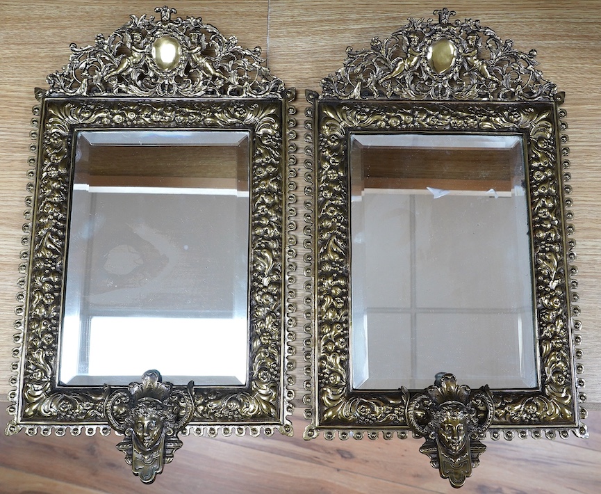 A pair of French brass repoussé mirrors with an ornate putti top and mask decorated bottom, 49cm high. Condition - good